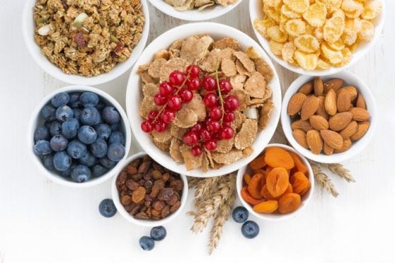 assortment of different breakfast cereal, dried fruit and fresh berries on white wooden table, top view, horizontal