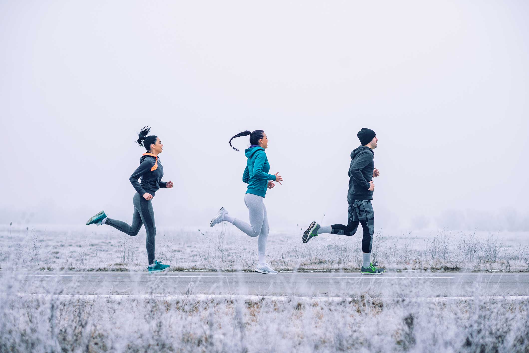 Three people jogging on road, winter background.