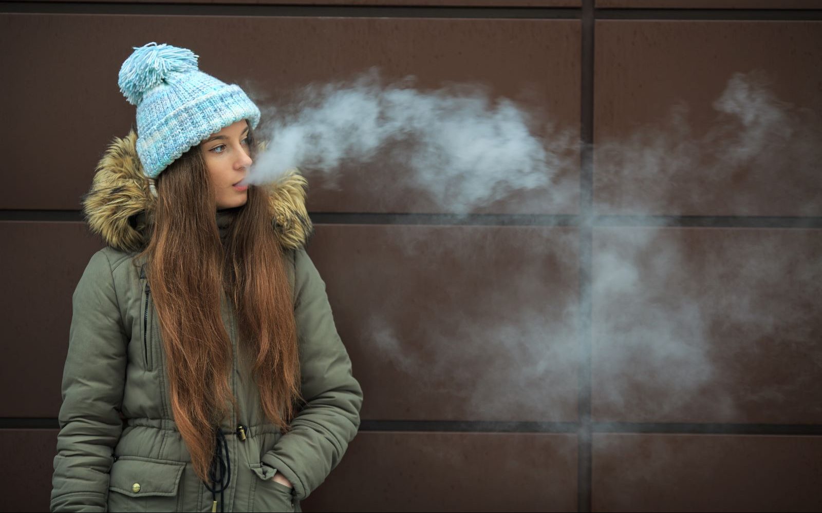 Teenage girl vaping against a wall.